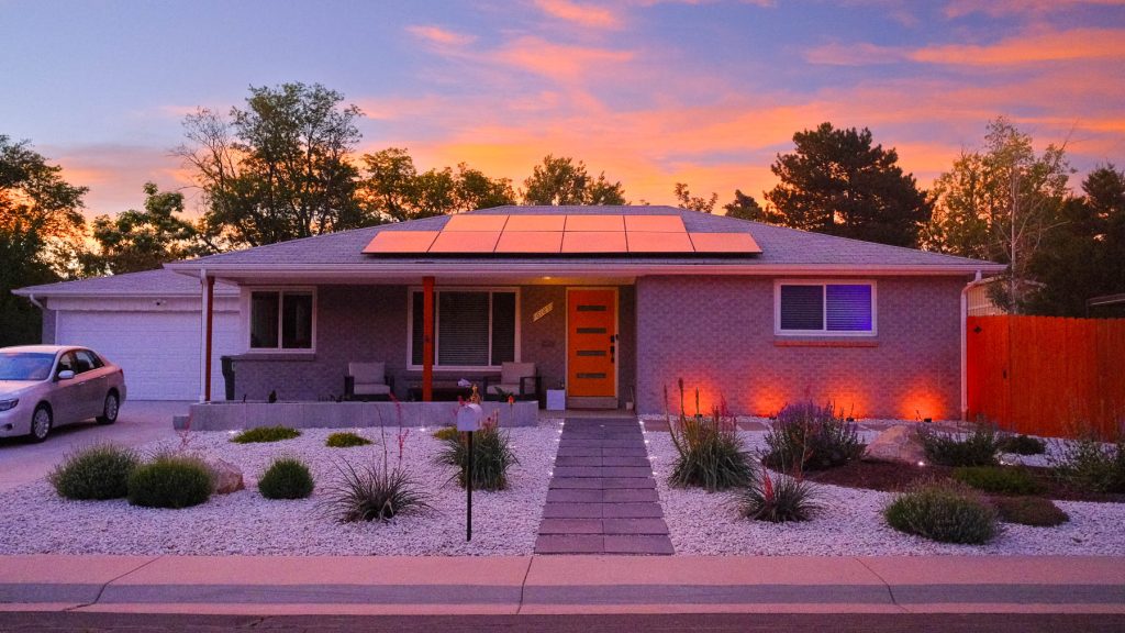 Denver ranch home with xeriscaped front yard featuring white rock, native plants, and landscape uplighting at dusk