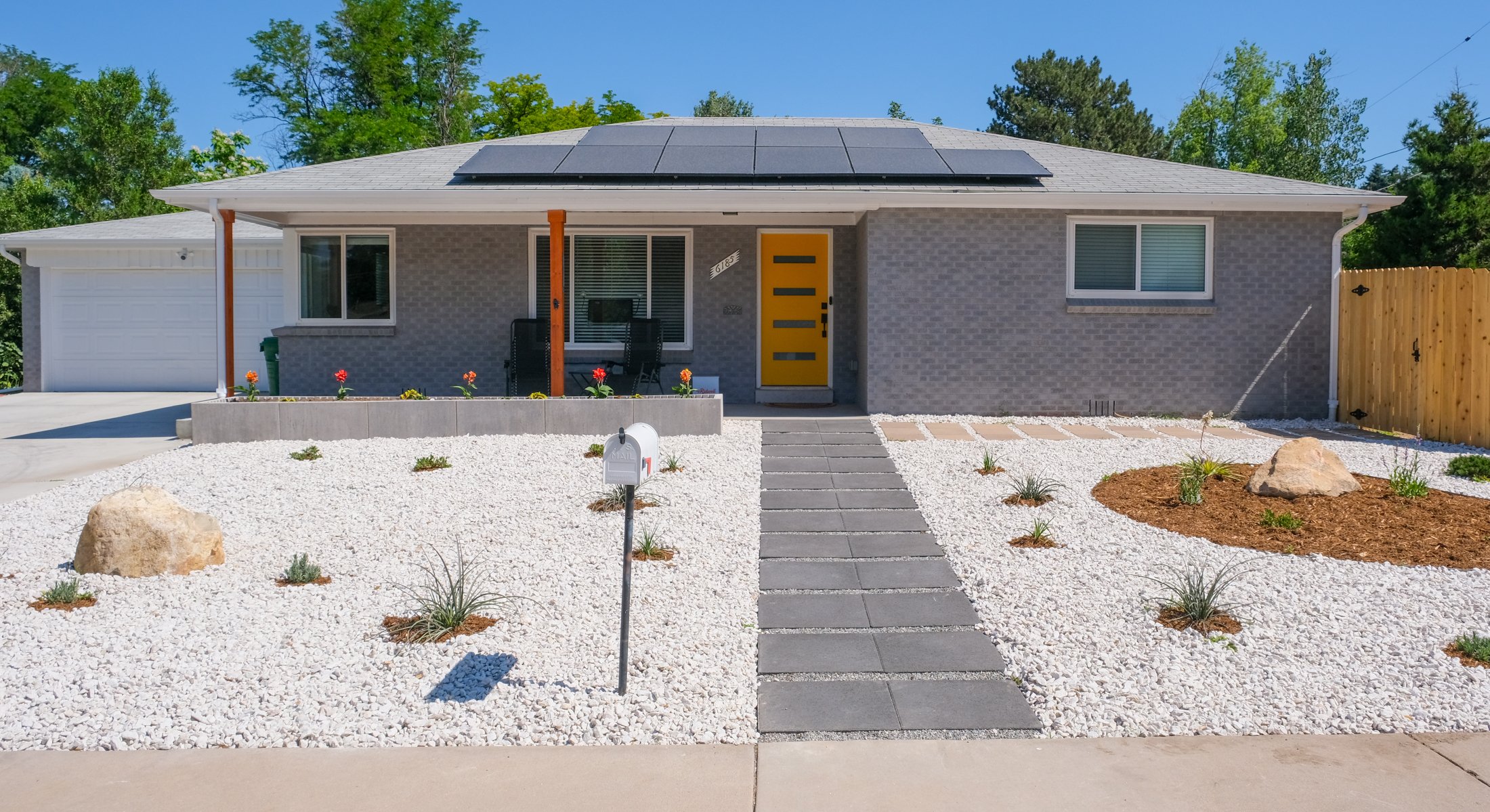 Grey House With Yellow Door and a Xeriscaped Landscape including white rocks and indigenous Colorado plants