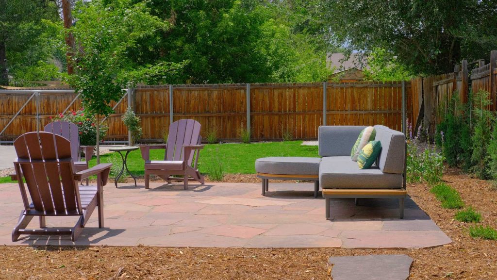 Flagstone patio in a West Denver landscaping project with a lounge sectional and Adirondack chairs surrounded by mulched planting beds